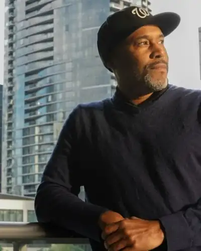 Jean Nicolas in a Washington Nationals cap, leaning on a balcony rail in front of city high-rises